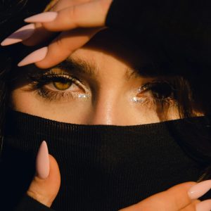 Close-up of a woman with glitter eyeshadow and pink nails, partially obscured by fabric. Fashionable and stylish portrait.