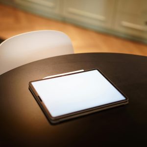 A tablet with a blank screen resting on a sleek black round table in a warm, modern kitchen setting.